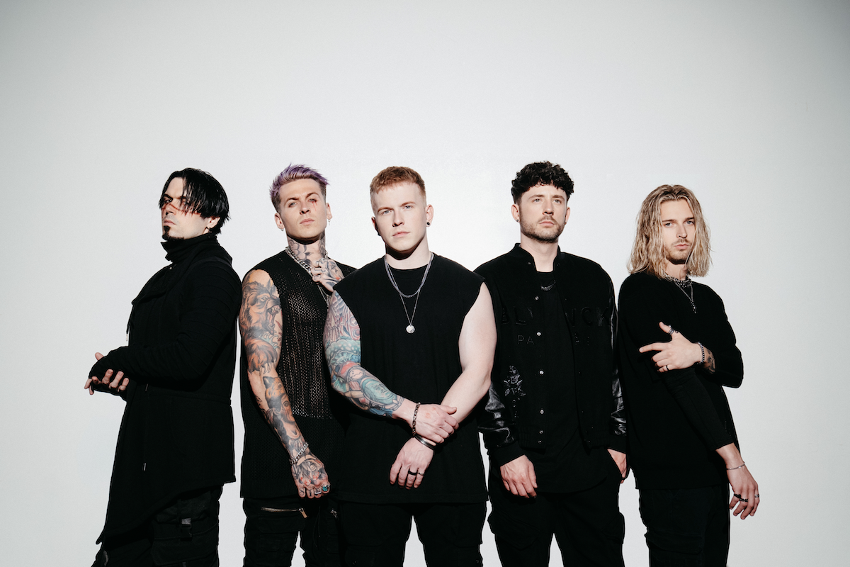 Rock band From Ashes to New standing together in dark clothing against a plain white background, photographed by Alex Bemis.